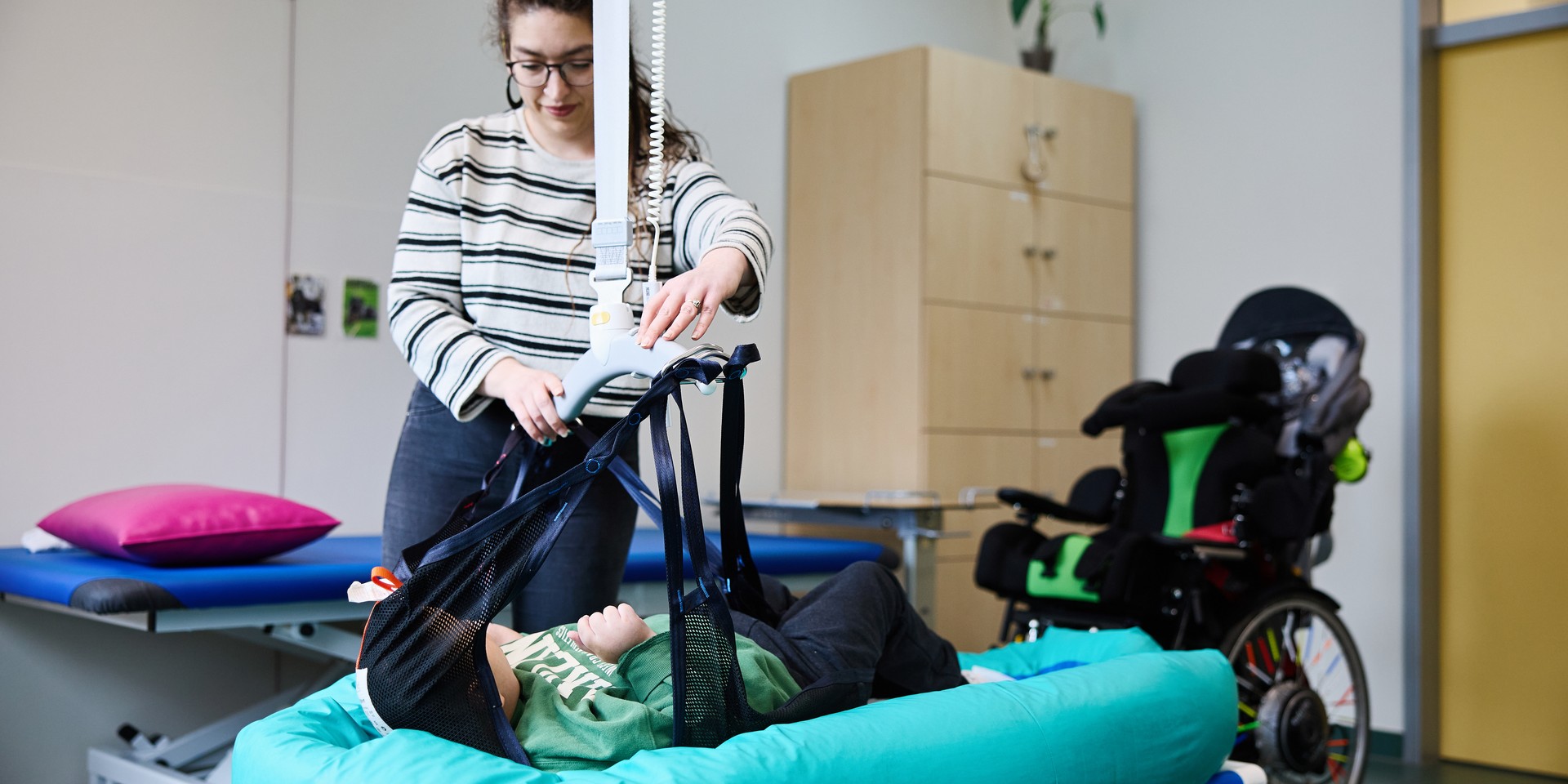 Bild zeigt Pflegekraft, die einen Schüler mit einem Lifter auf eine Liege legt.